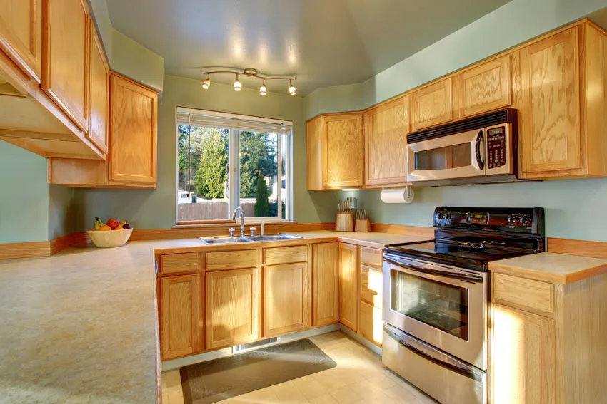Kitchen with green walls, honey oak cabinets, oven, ceiling lights, and windows