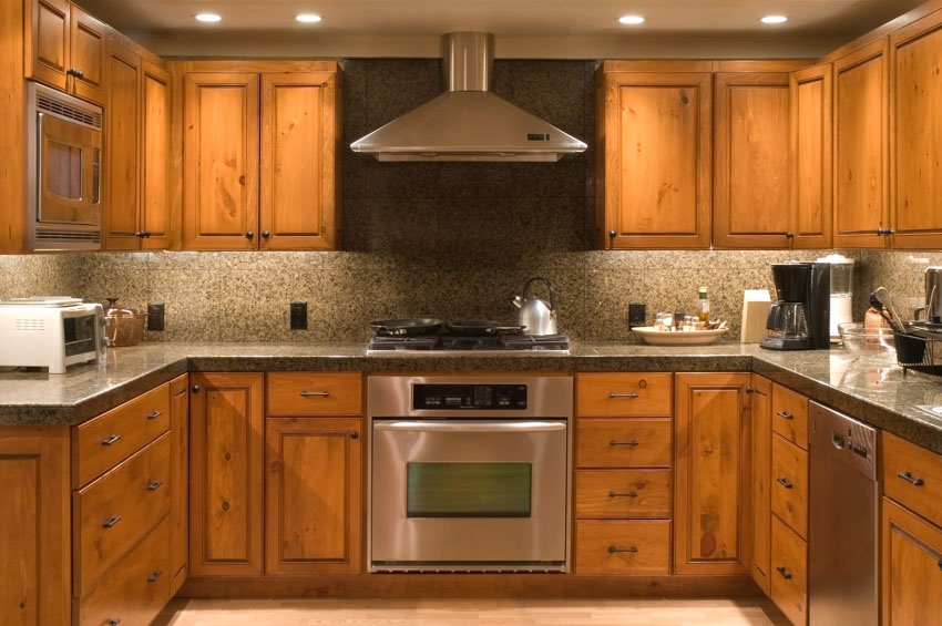 Kitchen with amber honey cupboards, granite speckled backsplash, range hood, and oven