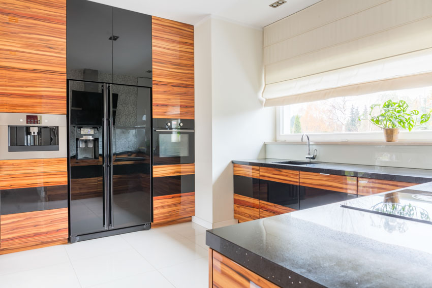 Kitchen with horizontal grain wood cabinets, countertop, black refrigerator, and windows