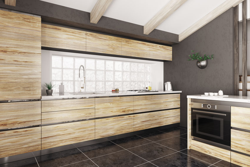 Kitchen with light wood horizontal grain cabinets, black tile floor, and glass backsplash