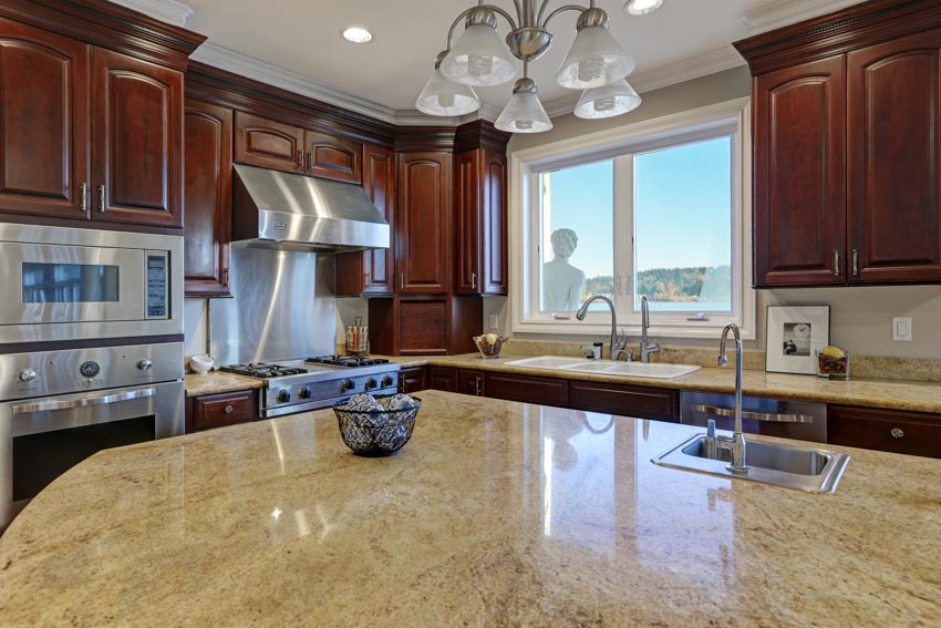 Kitchen with stained cabinets, granite countertops, sink, faucet, ceiling lights, and windows