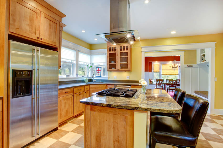 Kitchen with honey oak cabinets, tile flooring, island, tile flooring, range hood, stove, chairs, and yellow walls