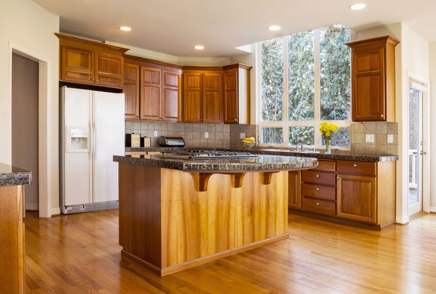 Kitchen with wood floor, stained cabinets, center island, floating countertop, and windows