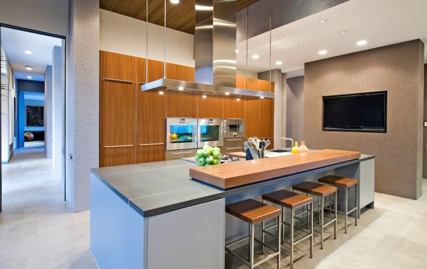 Large island with grey and wood overlay countertops, barstools, and range hood in a modern kitchen