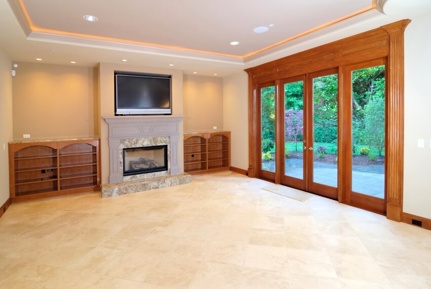 Large unfurnished room with fireplace, shelves, French door, and limestone flooring