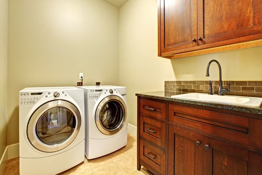 Room with dark brown cabinets, travertine tiles on the floor and black faucet