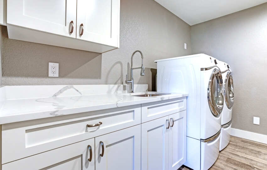 Laundry room with taupe walls, white cabinets, and marble top counters