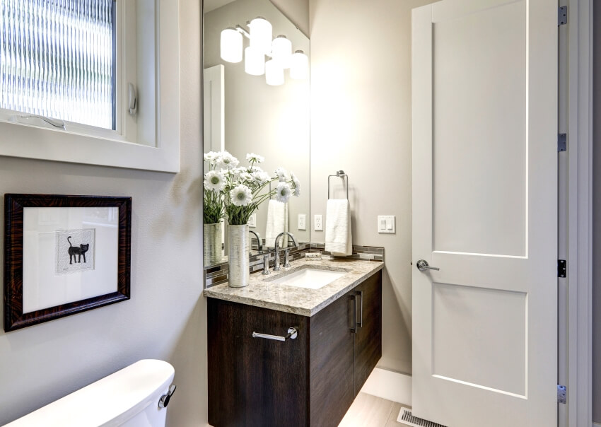 Light gray bathroom interior with dark wood corner vanity cabinet with granite counter