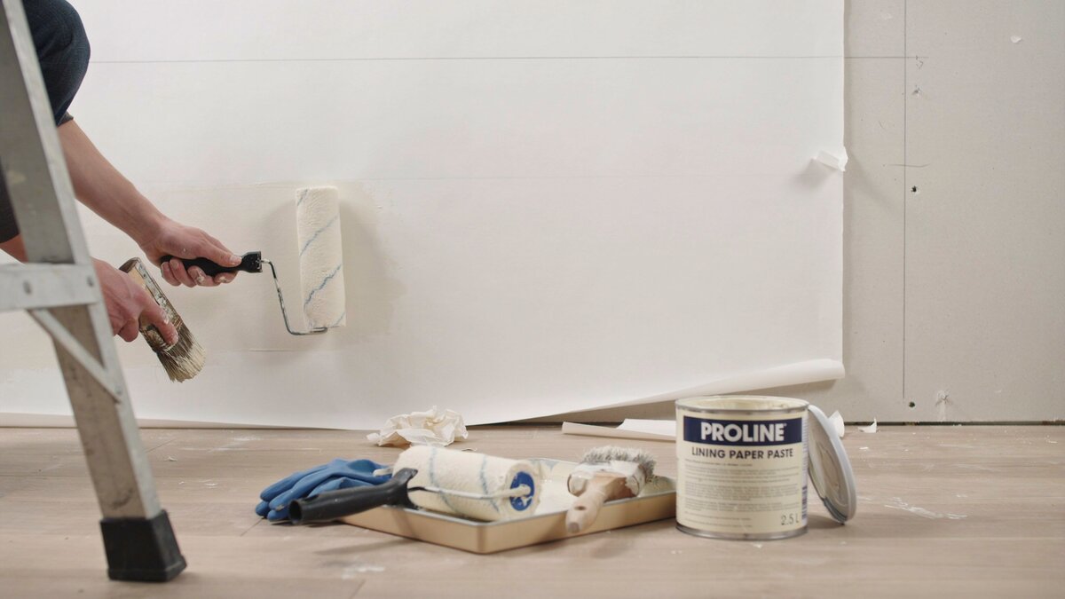 Person rolling white lining wallpaper onto a wall to smooth it