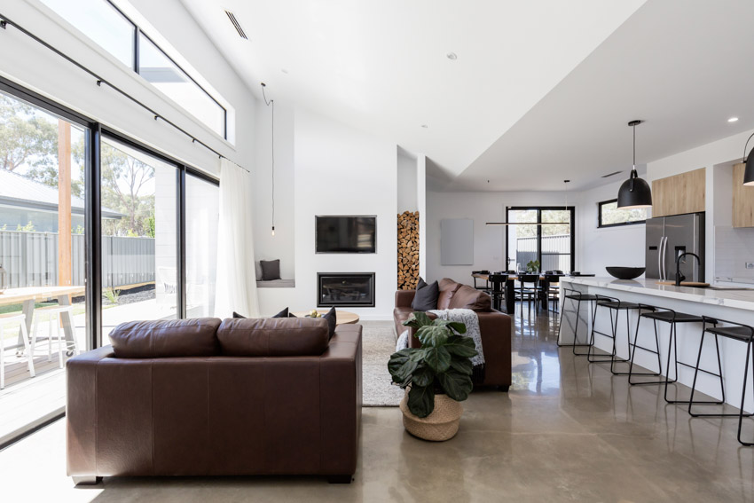 Living room with concrete overlay, glass window, kitchen bar, stools, sloped ceiling, and pendant lights