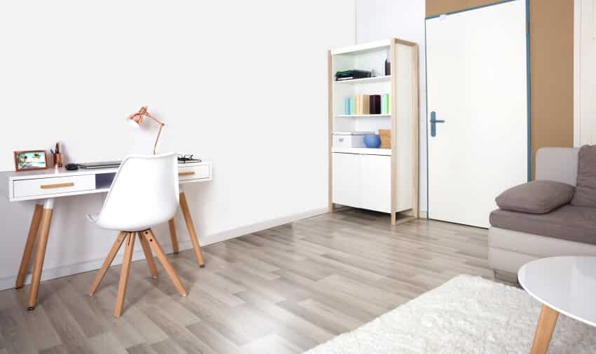 Living room with grey vinyl floor, standing shelf cabinet, and wooden working chair and table