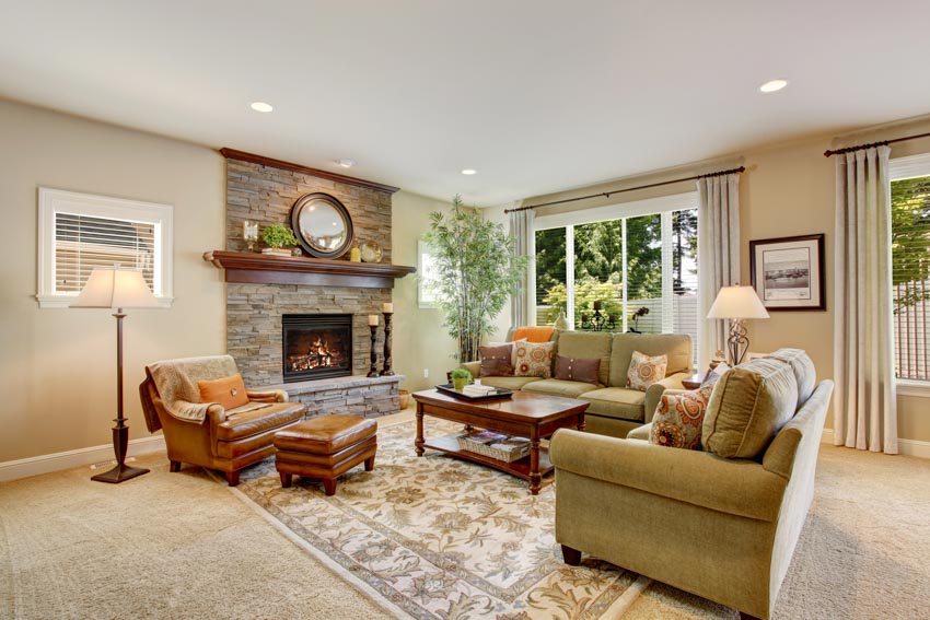 Living room with leather hassock, sofa chairs, coffee table, fireplace, floor lamp, windows, and ceiling lights