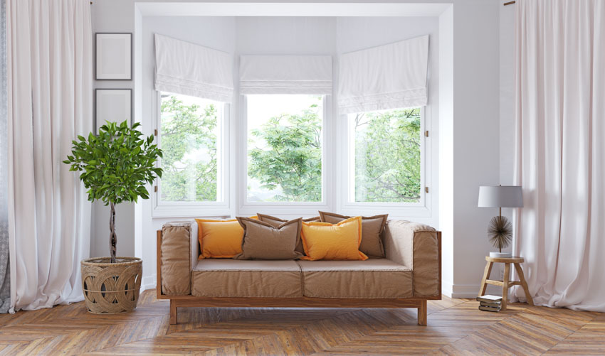 Living room with wood flooring, couch, cushion, lamp, potted indoor plant, curtains, and bay window