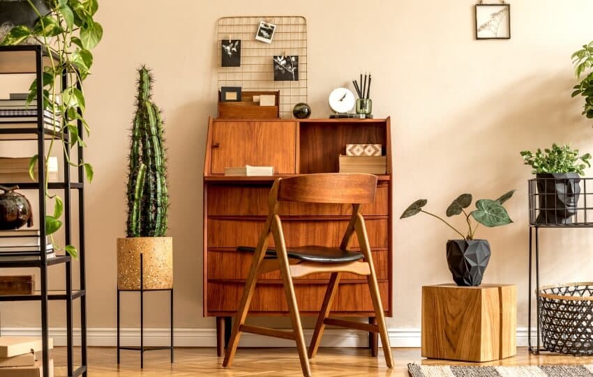 Living room with wooden vintage bureau, standing shelf, plants, decoration ,and beige wall