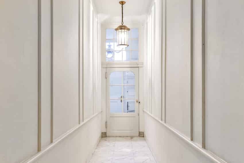 Long empty narrow hallway with white walls, tile floor, and pendant light