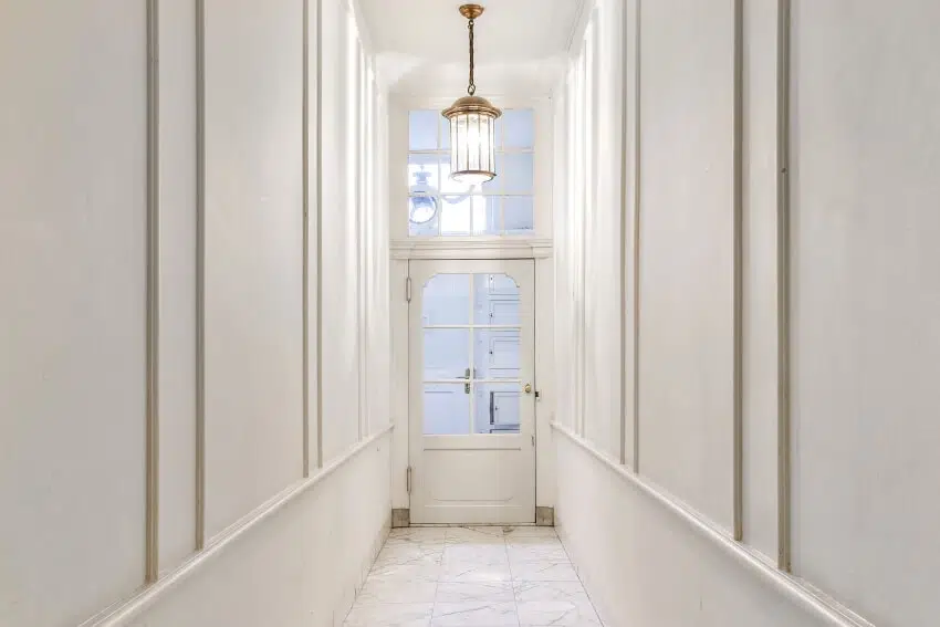 Long empty narrow hallway with white walls, tile floor, and pendant light