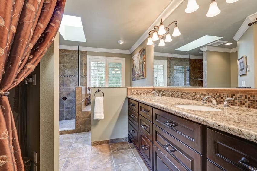 Luxurious bathroom with granite countertop, wood drawers, accent lights, mirror, and skylight