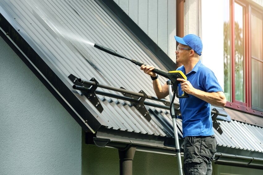 Man standing on ladder and cleaning house metal roof with high pressure washer