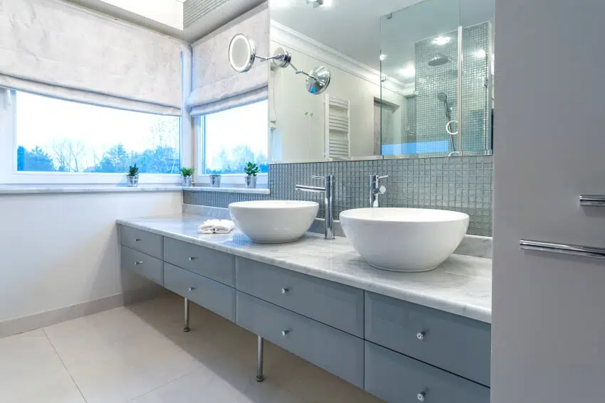 Modern bathroom interior with two sinks, glass tile backsplash, marble countertops, and windows