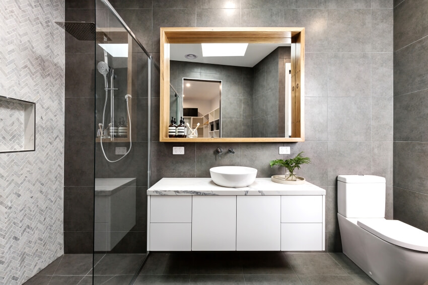 Modern grey bathroom with herringbone shower tiling, and a floating vanity with wood framed mirror