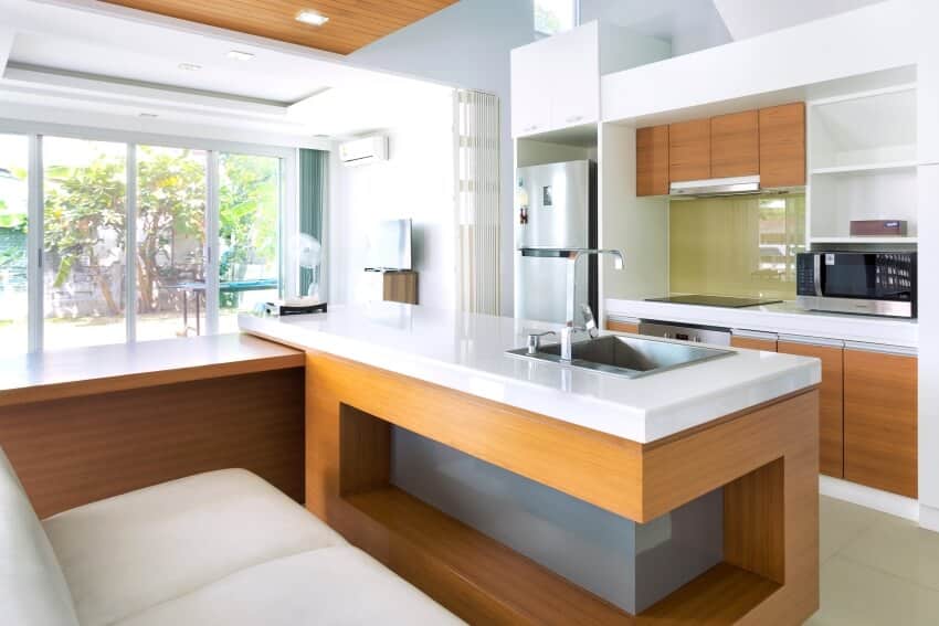 Modern kitchen with wood cabinets, and wooden bar counter covered with white countertops and seating bench