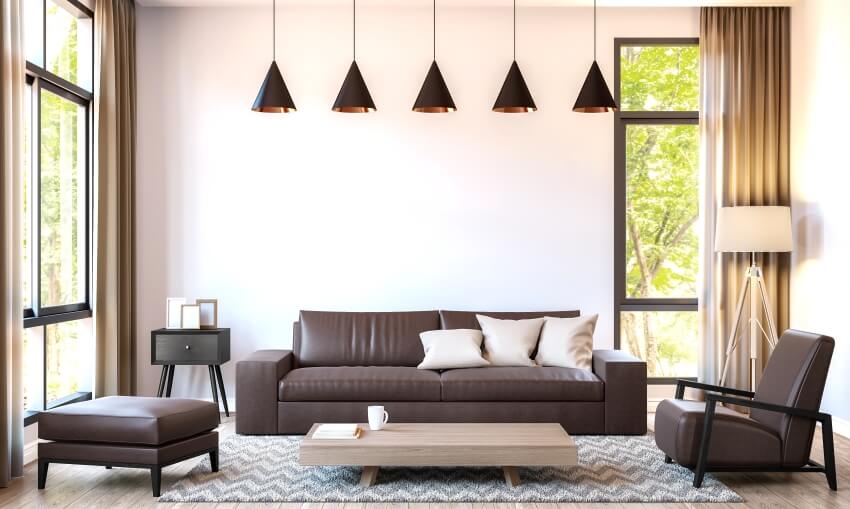 Modern living room with dark brown leather furniture, pendant lights, and large windows