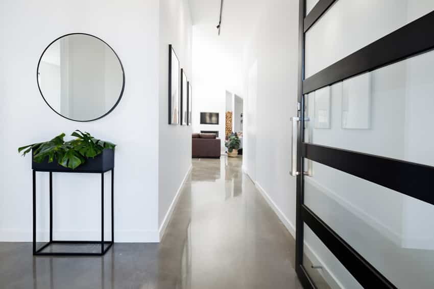 Narrow hallway with polished concrete floor, mirror, and glass door