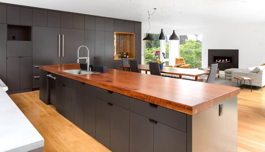 Open modern kitchen with grey cabinets, and large island with varnished wood countertop