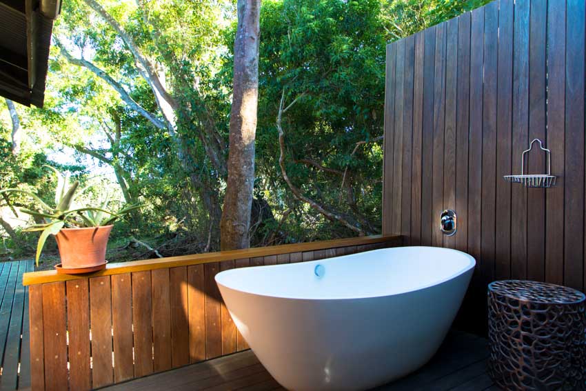Outdoor area with bathtub, wood wall, faucet, and railing