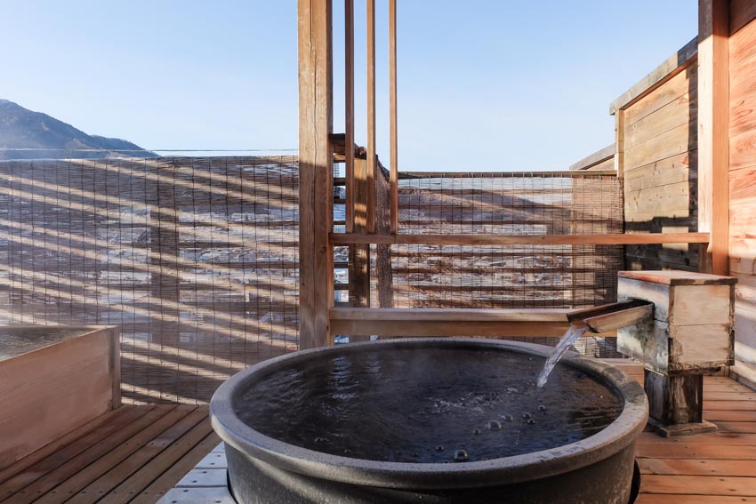 Outdoor bath with black tub, wood flooring, and water supply