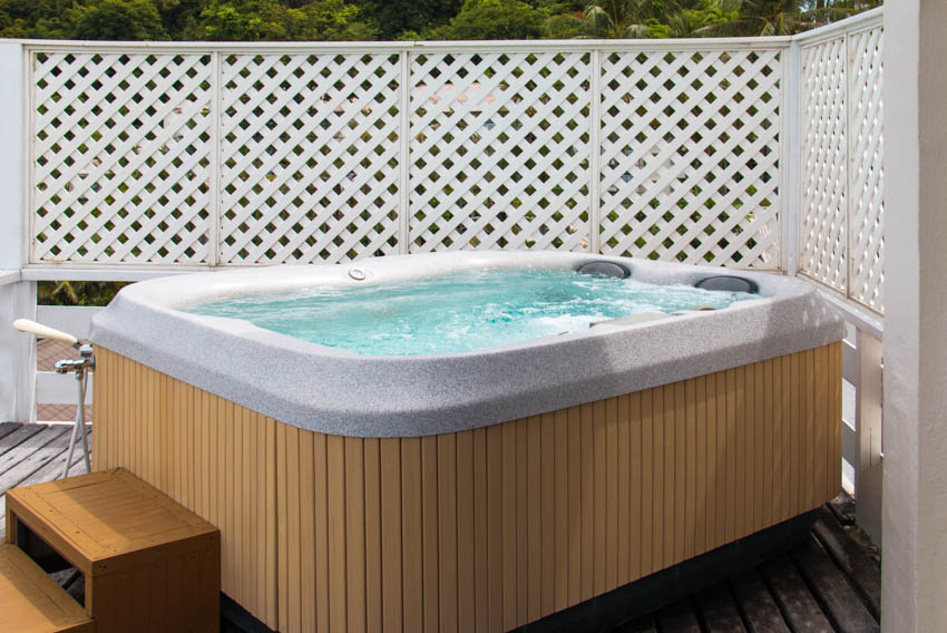 Outdoor bath with hot tub, lattice fence, and wood steps