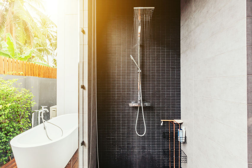 Outdoor bath with tub, modern shower, black tile wall, and plants