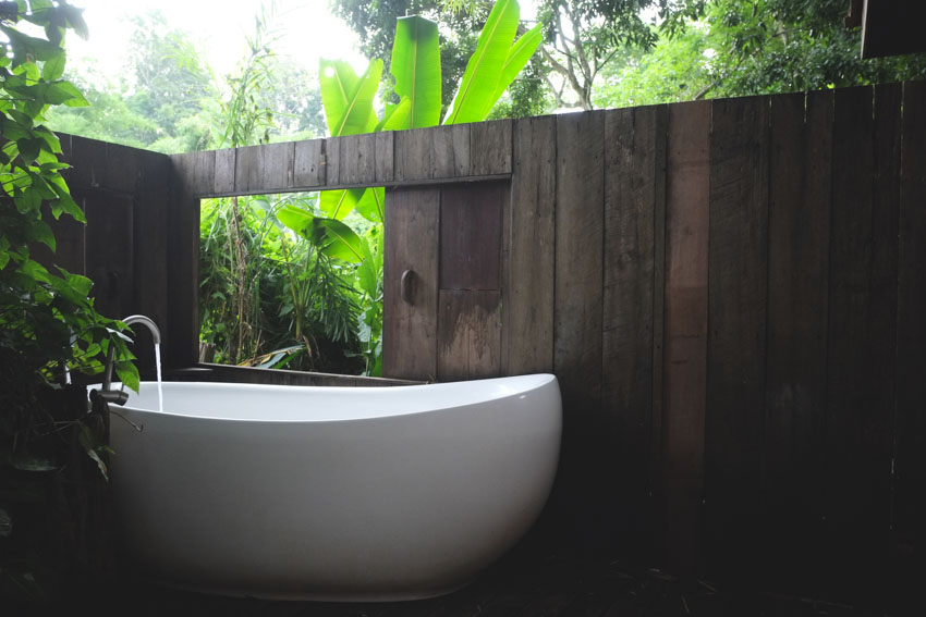 Outdoor bath with white tub, wood fence, and plants