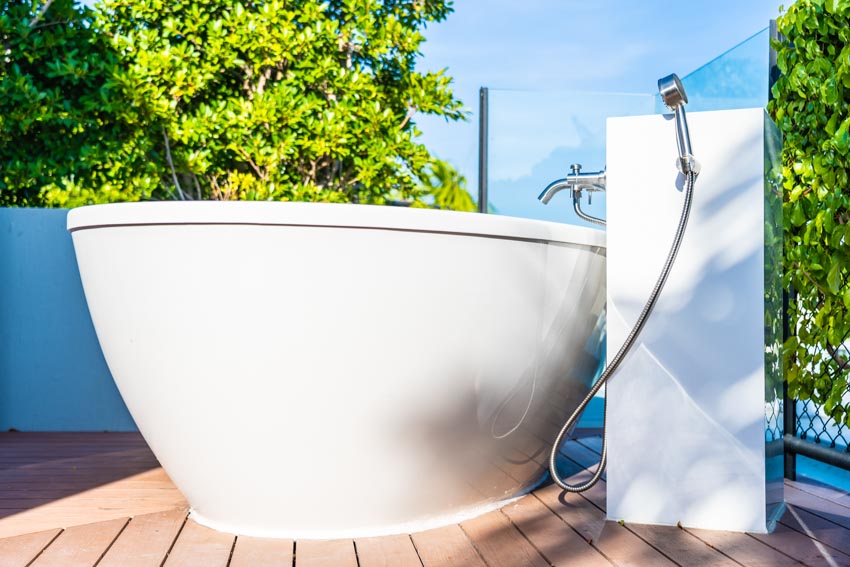 Outdoor bathroom with white tub, faucet, wood flooring, and showerhead