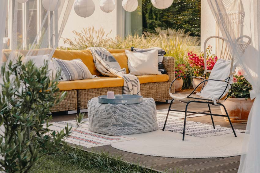 Outdoor deck area with couch, chair, pillows, ottoman, and floor rug