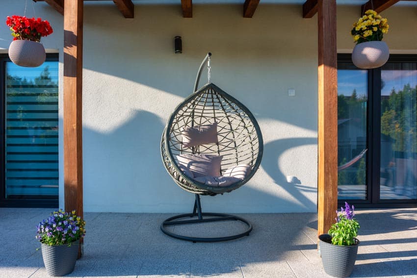 Egg chair with stand on covered concrete patio with wood beams and potted flowers