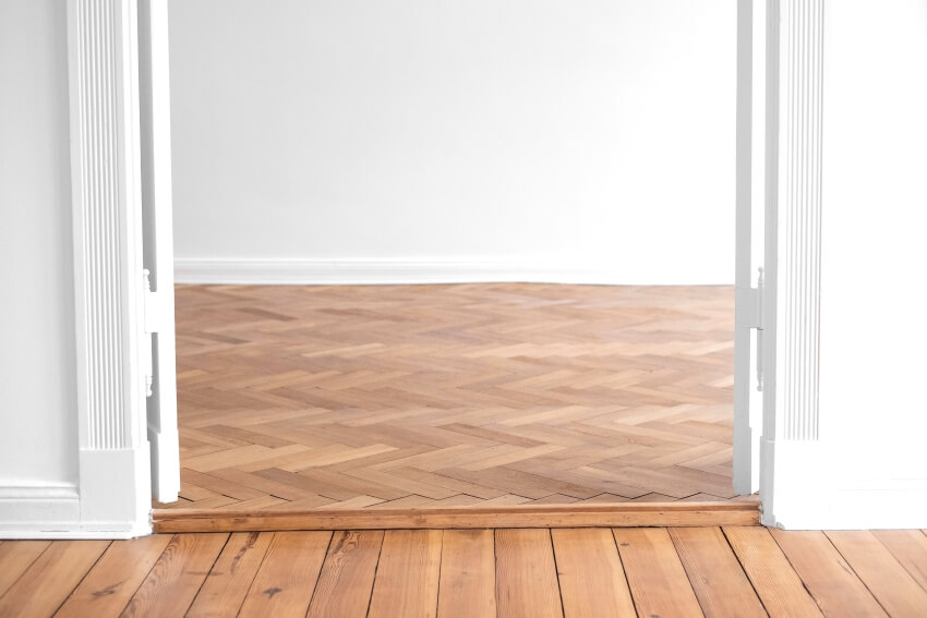 Parquet to wood panel floor transition in empty apartment room with open double wing door