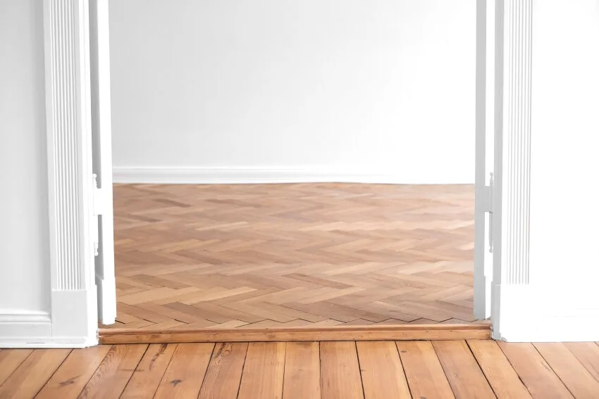 Parquet to wood panel floor transition in empty apartment room with open double wing door