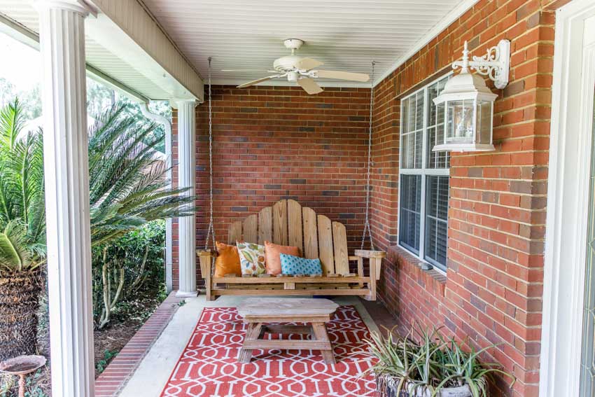 Patio area with hanging chair made of wood, small table, brick wall, and outdoor rug