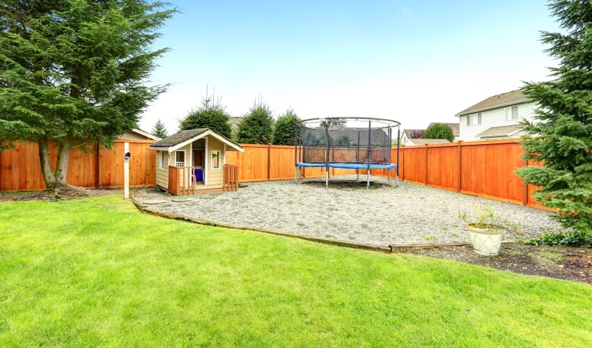 Playhouse and trampoline in a wood fenced backyard