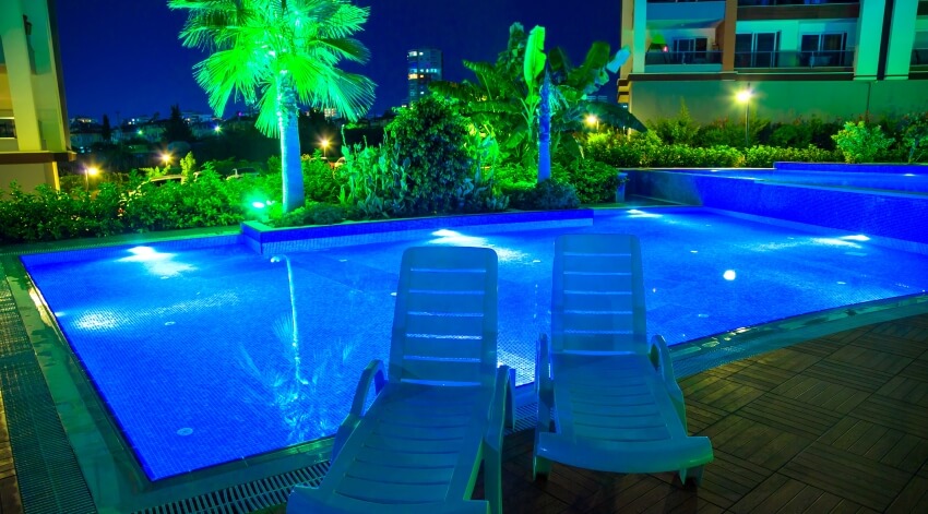 Residential pool at night with LED lights and two sun lounger