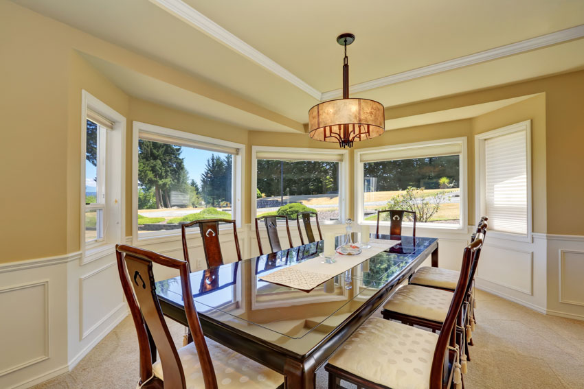 Room with long dining table, wainscoting, hanging light, chairs, and windows