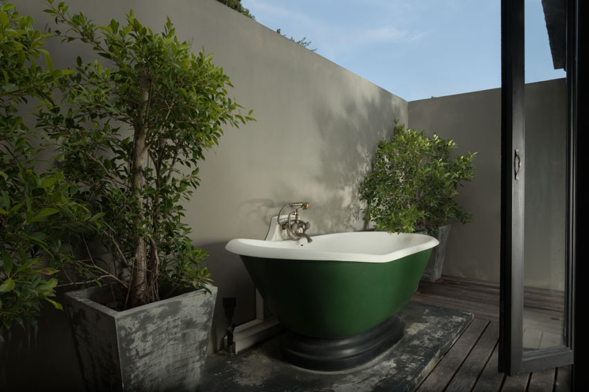 Secluded outdoor bath with green tub, wood flooring, and plants