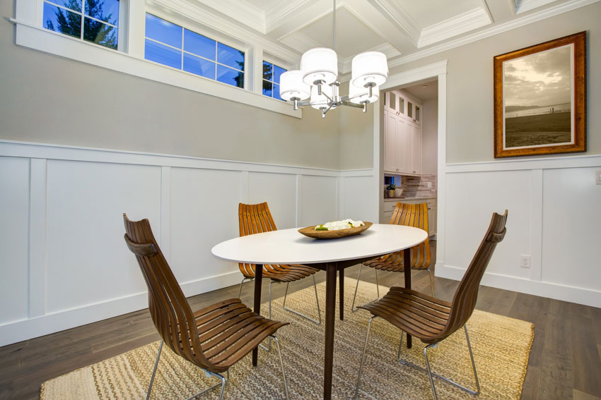 Simple dining area with table, chairs, floor rug, wainscoting, and windows