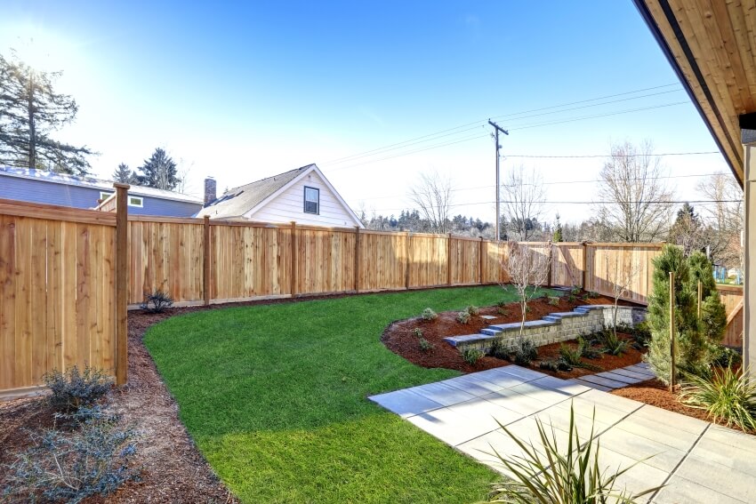 Sloped backyard surrounded by pine wood fence with tiled walkway and green lawn