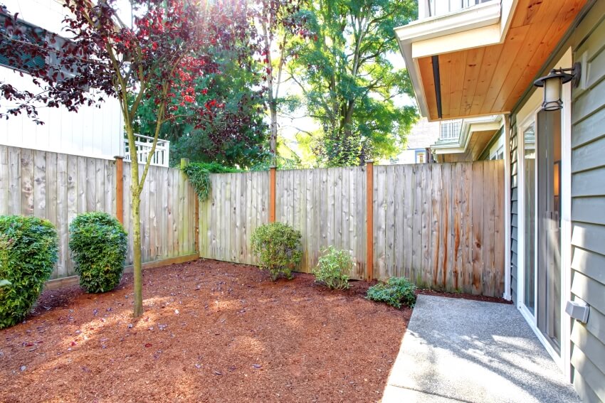 Small backyard area with sawdust and high wooden fence