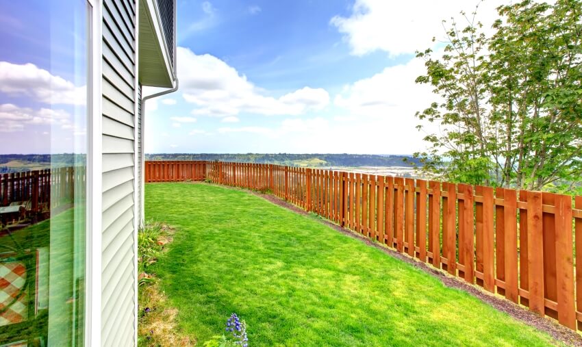 Small redwood fenced backyard of a large blue house with grass filled garden and amazing view
