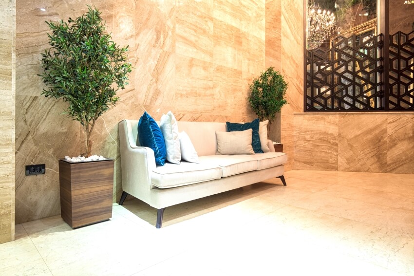 Sofa in between large potted plants in a lobby with stone tile walls and floor