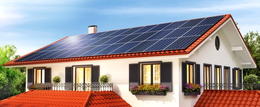 Solar panels on the red roof of a beautiful house with exterior window shutters