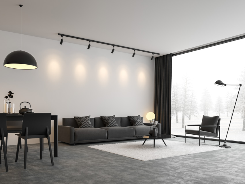 Spacious living room with track lights, couch floor, lamp, table, chairs, window, and concrete floor